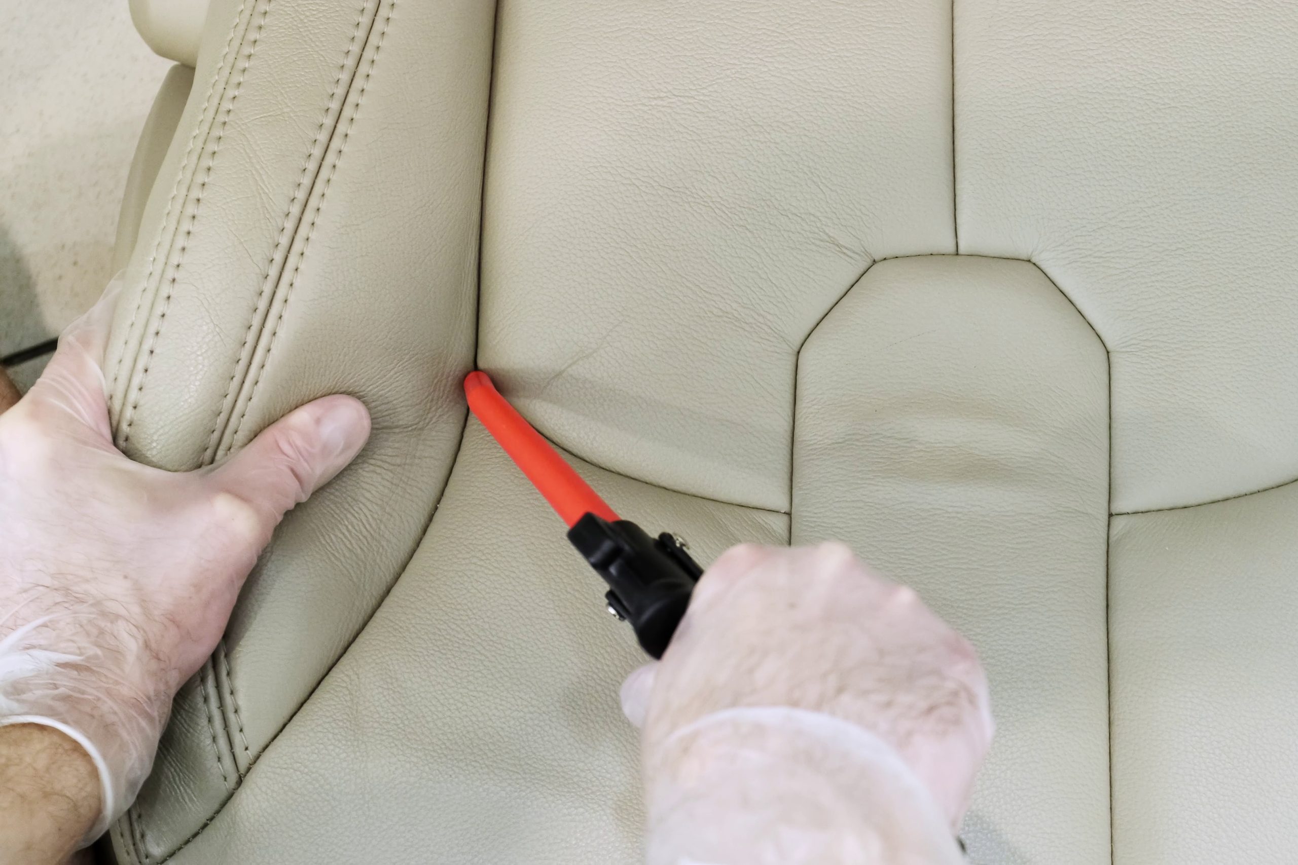 Detailing of the interior of a modern car. A man inflates the wrinkles on a beige car seat with a compressor. Car cleaning specialist. View from above